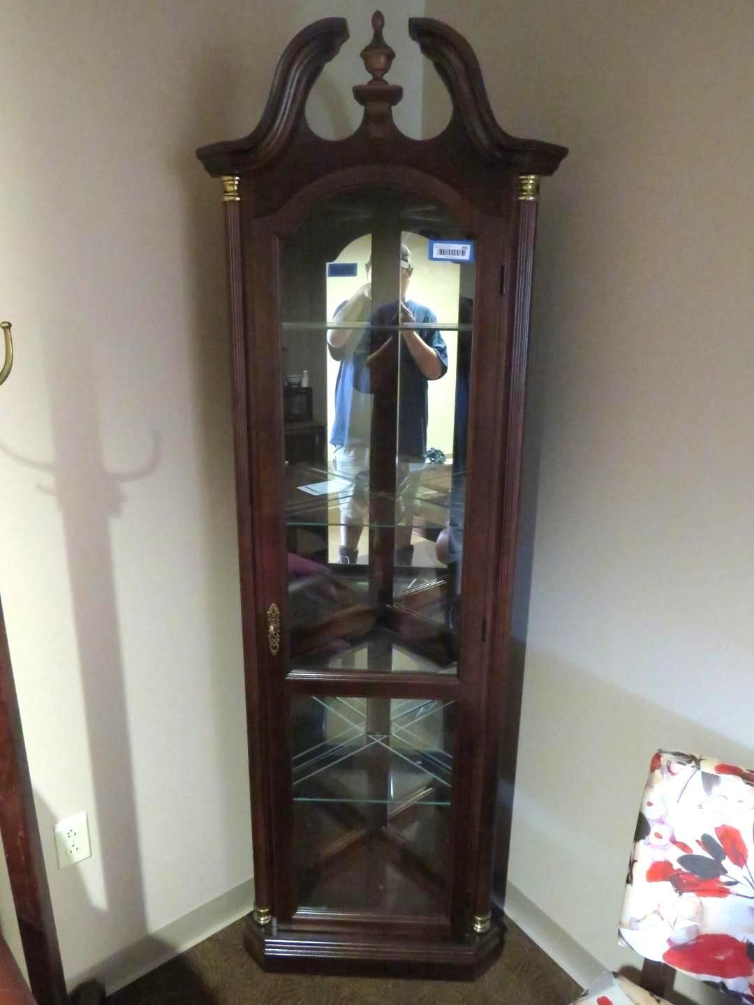 Dark wood corner cabinet with glass door and shelves, in a room.