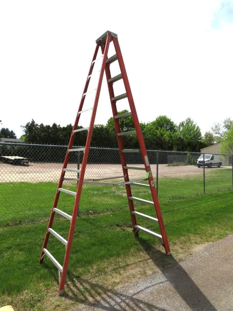 Red A-frame ladder set up on grass.