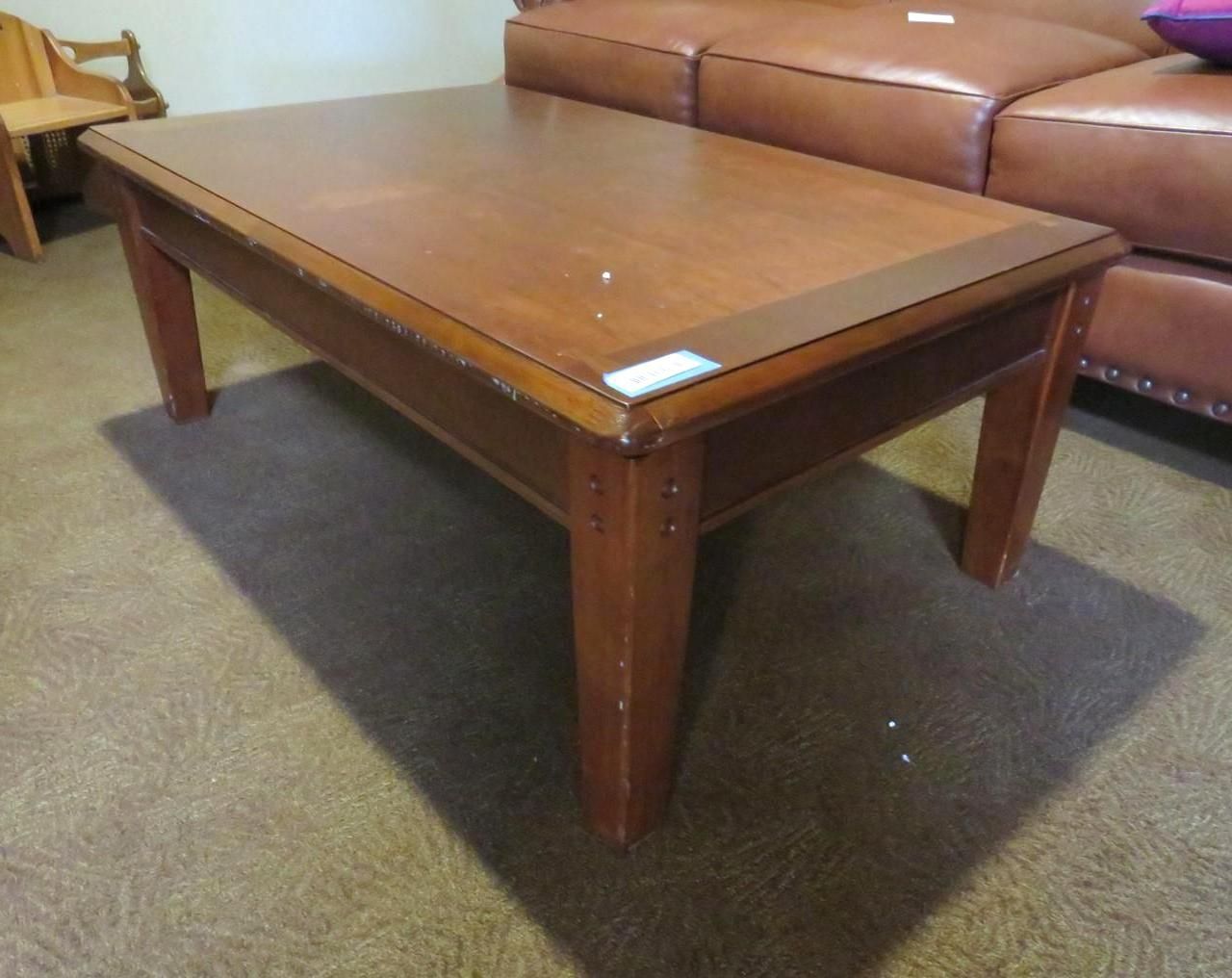 Wooden rectangular coffee table, brown color, in front of a brown leather sofa.