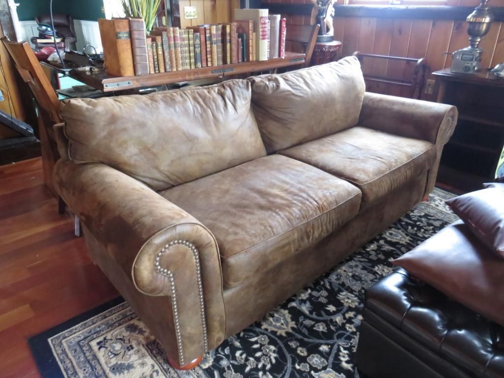 Brown leather sofa in a room, with a dark patterned rug and books on a shelf in the background.