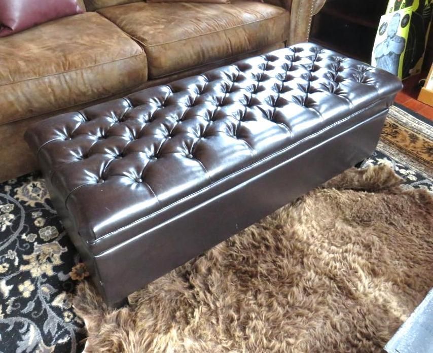 Brown tufted storage ottoman on a brown fur rug, next to a brown leather sofa.
