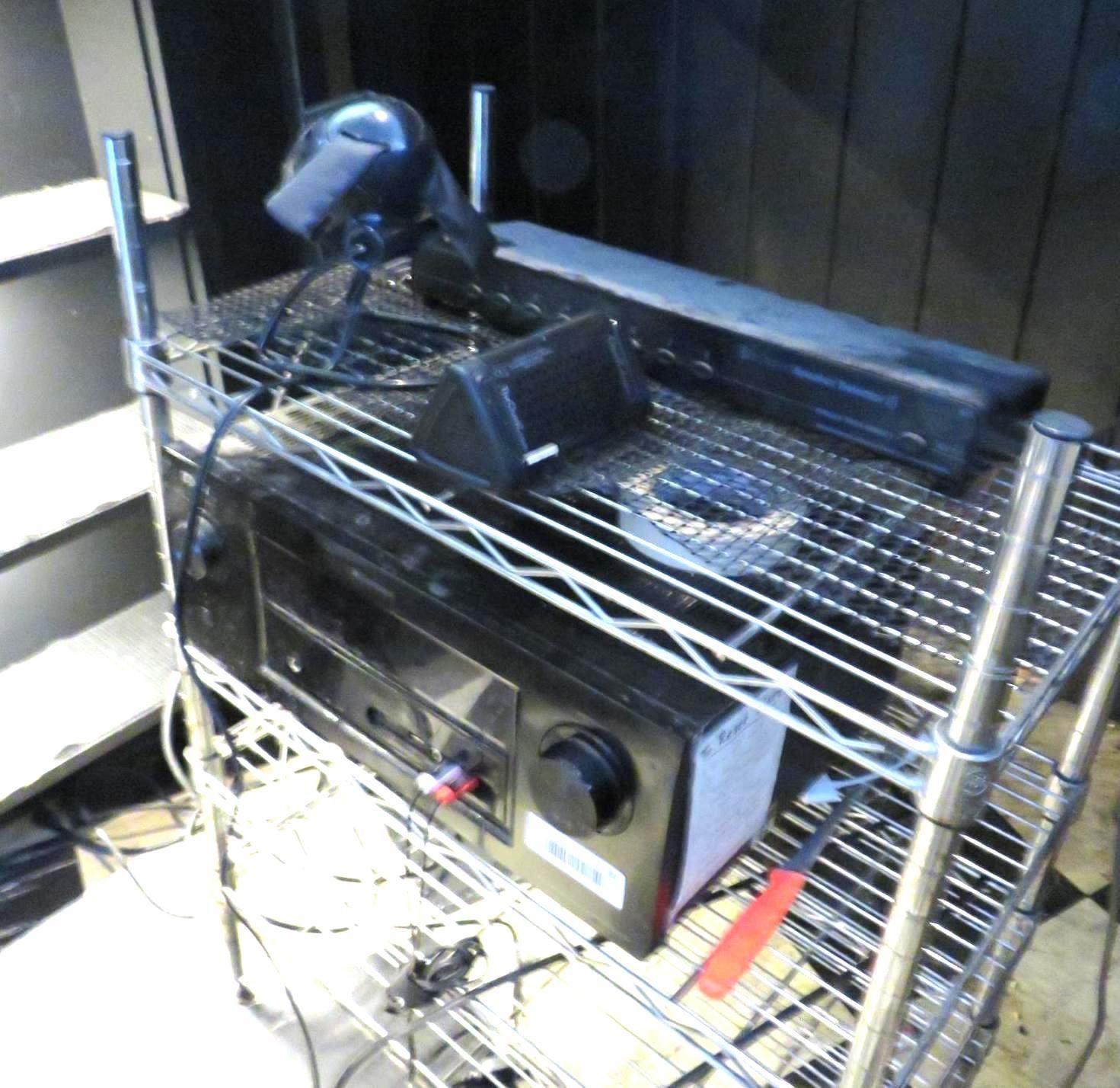 Black audio equipment on a metal wire rack in a dark room. Various cables and accessories are present.