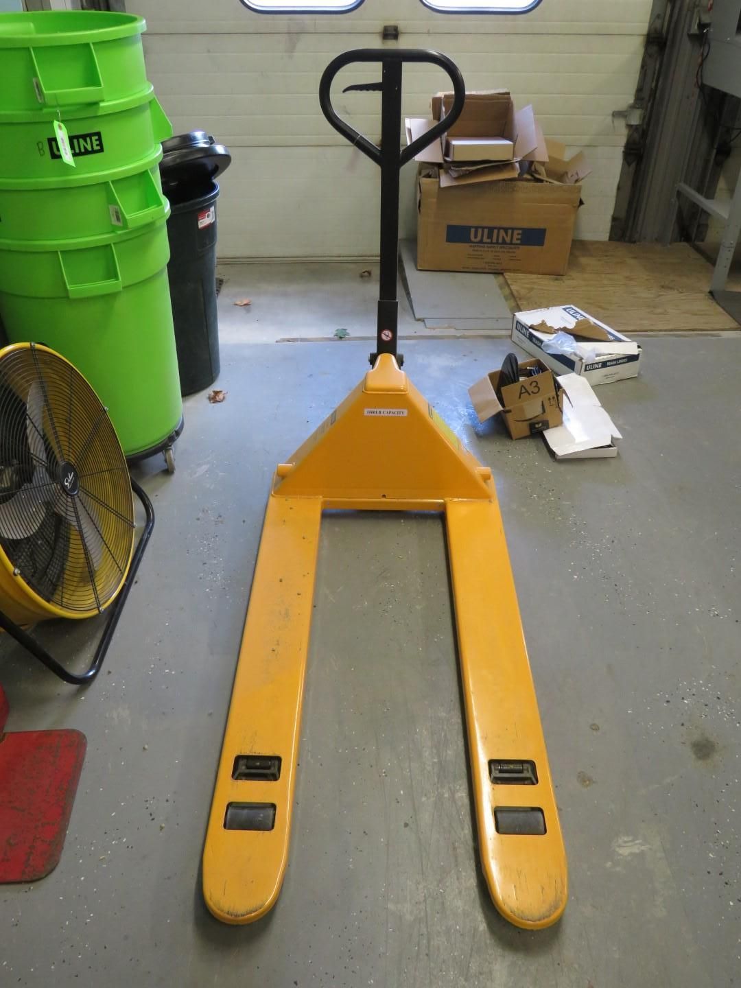 Yellow pallet jack with a black handle on a gray floor.
