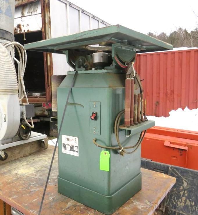 Green industrial table saw on a metal surface, outdoors.