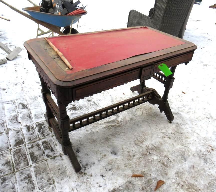 Antique wooden desk with a red top and ornate detailing.