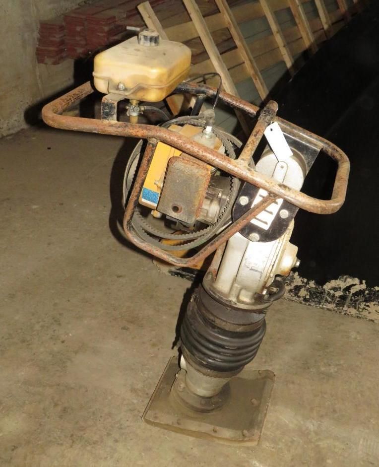 A gas-powered plate compactor with a yellow engine and tan fuel tank in a garage.