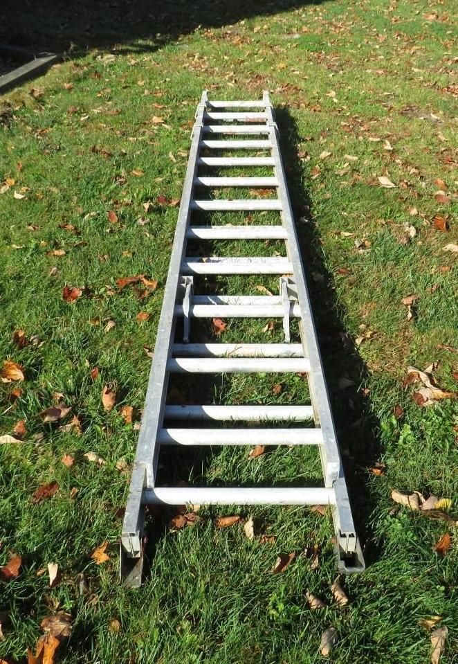 Aluminum extension ladder lying on grass.