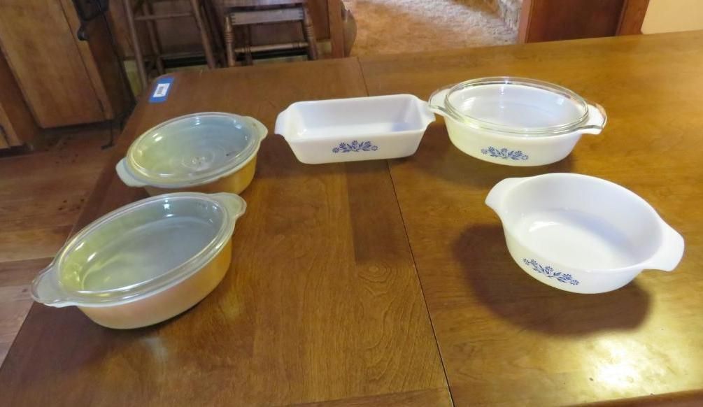 Several white and light yellow CorningWare dishes with blue floral patterns on a wooden table.