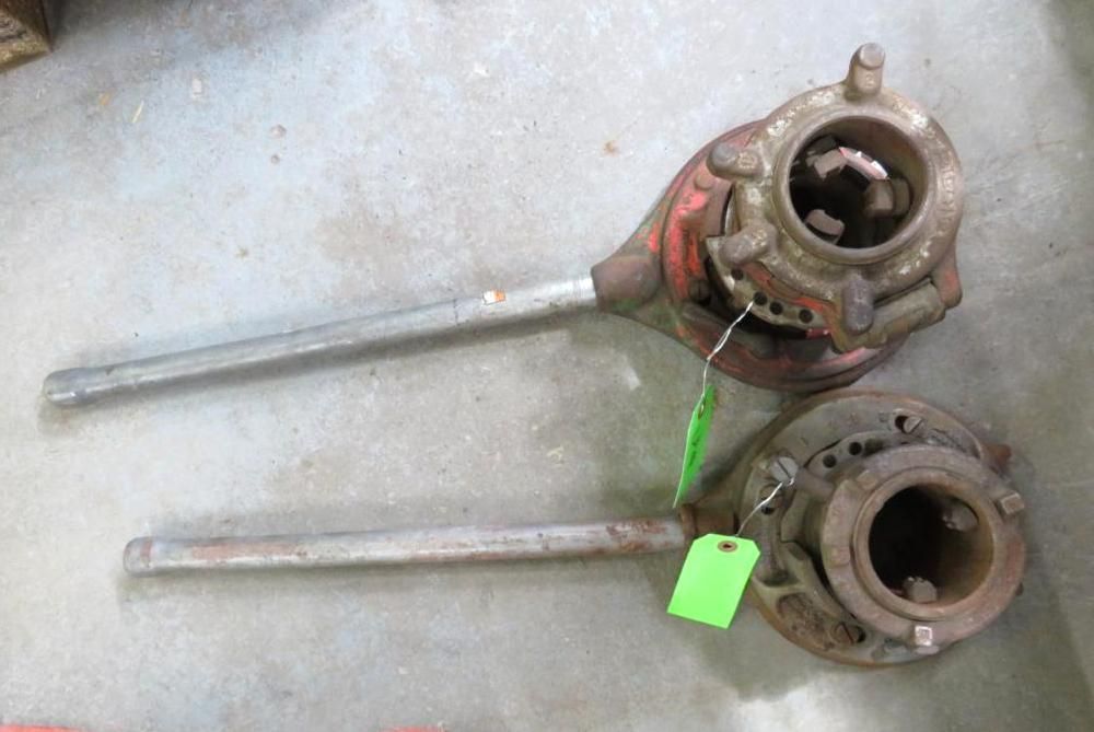 Two pipe threading tools on a concrete surface. One red, one brown, both with silver handles.