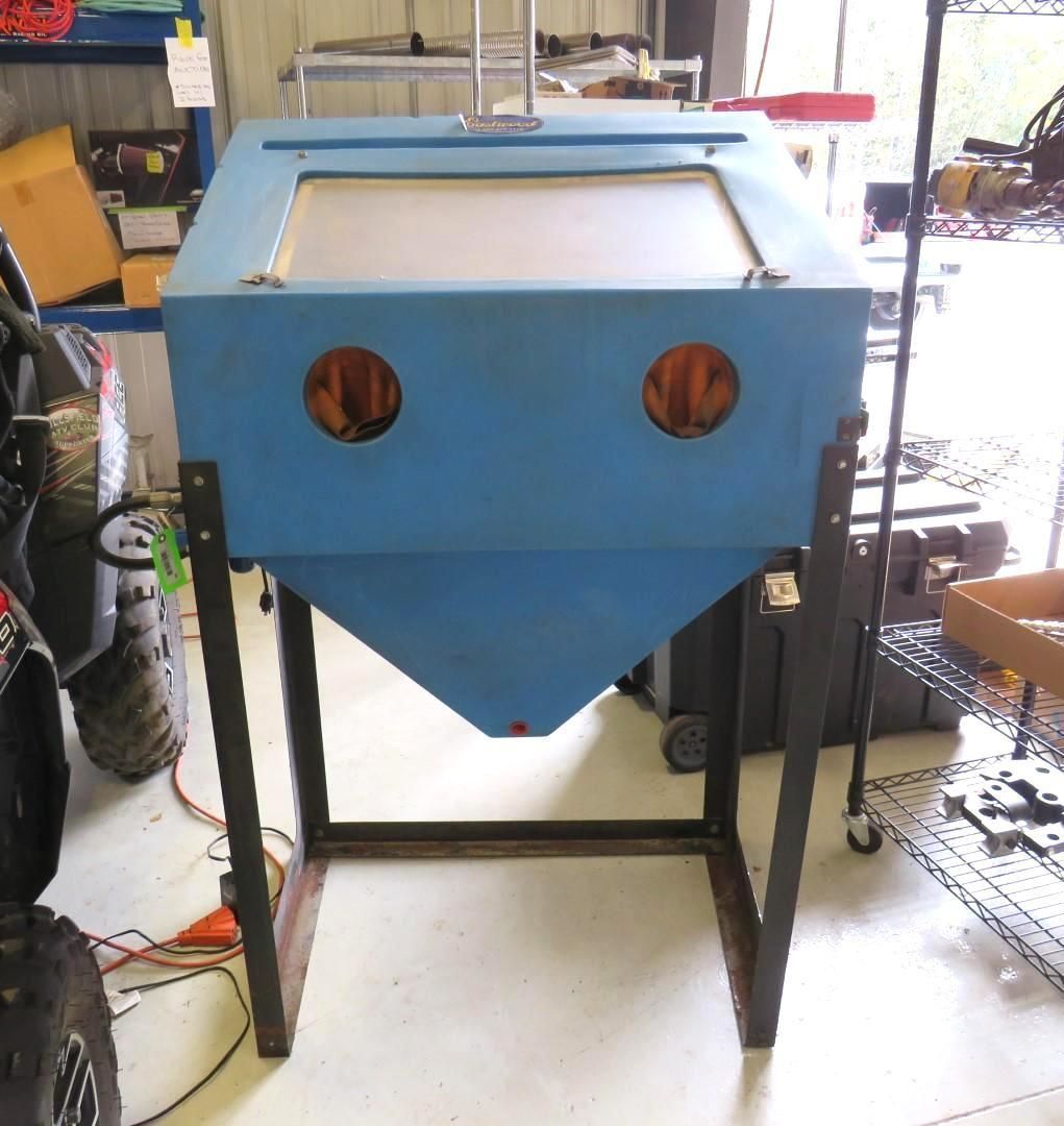 Blue sandblasting cabinet on a metal stand in a garage.