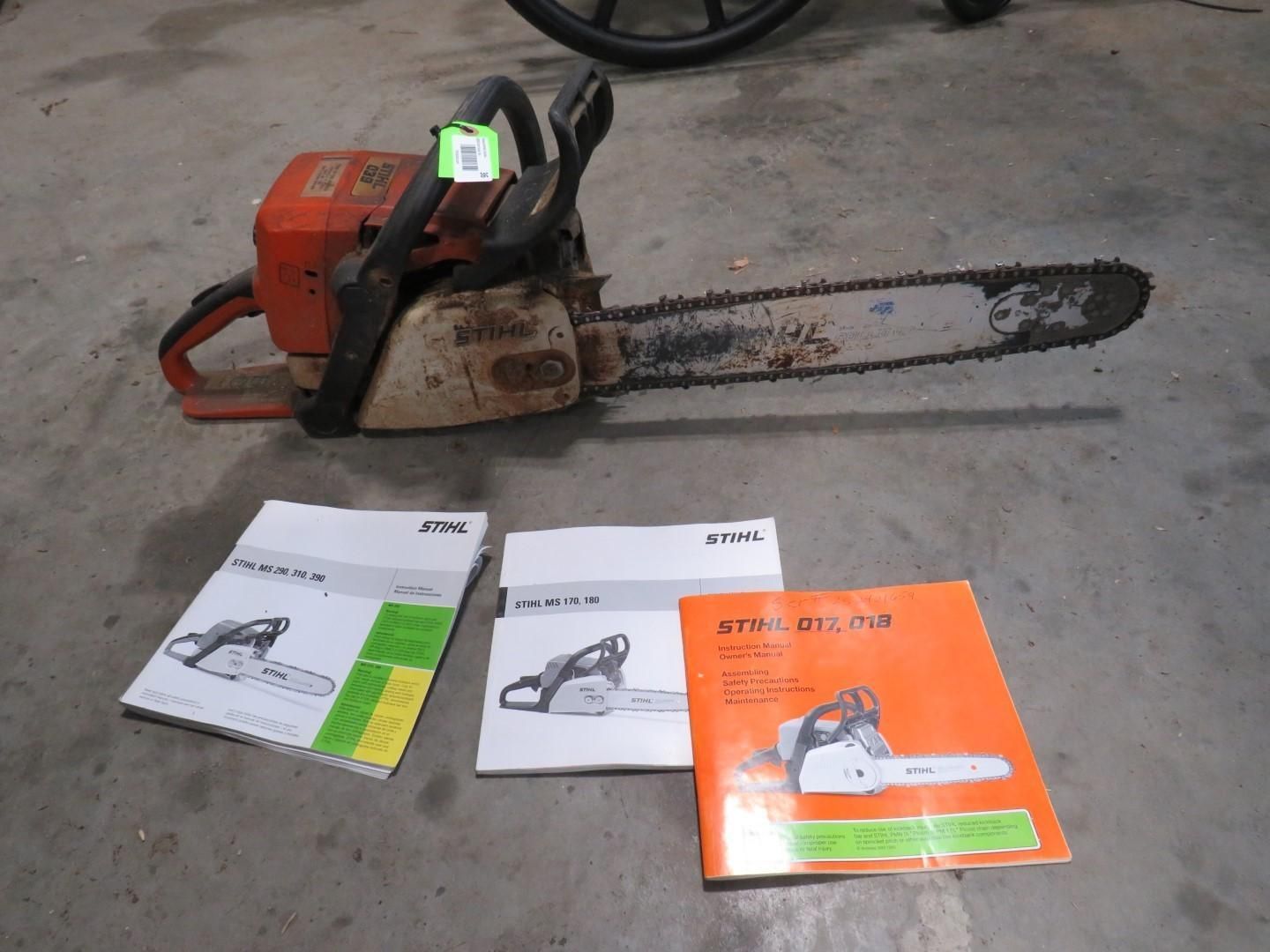 Orange and white chainsaw with three instruction manuals on a concrete surface.