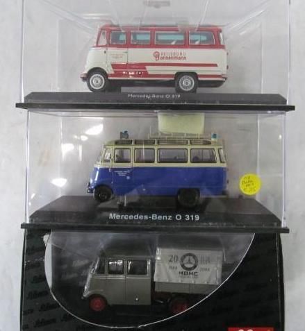 Three model Mercedes-Benz O 319 vans in display cases; red/white, blue/cream, and grey/white with a trailer.