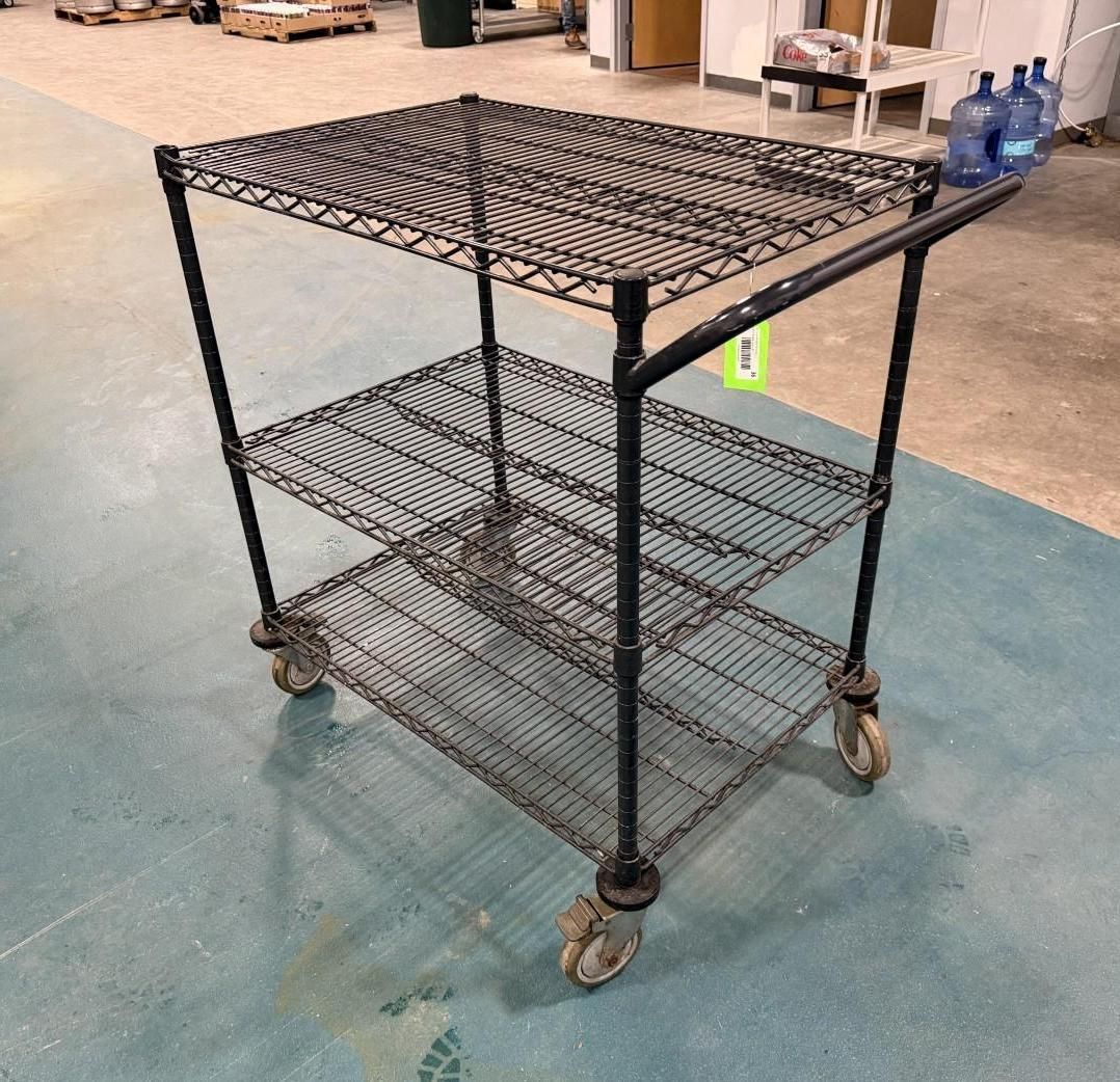 Black wire shelving cart with three levels, on wheels, in a warehouse.