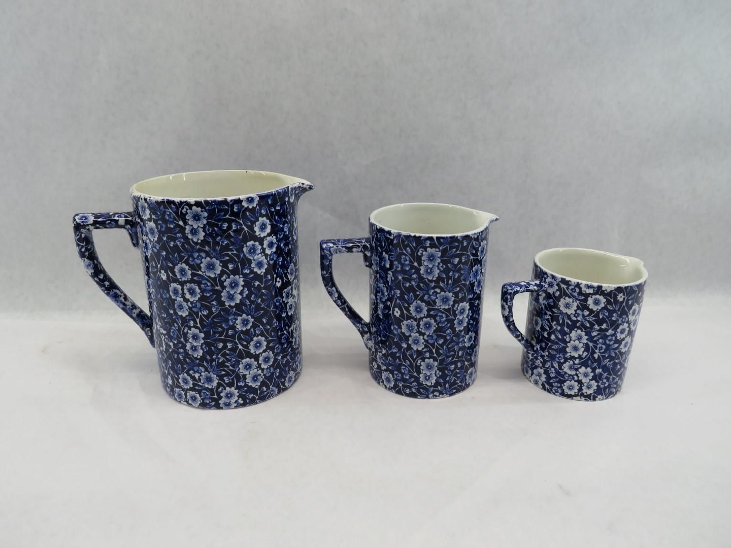 Three blue and white floral-patterned ceramic pitchers of varying sizes arranged from large to small.