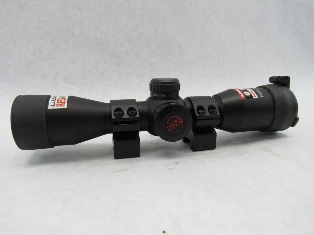 Black rifle scope with a red logo on a white surface.