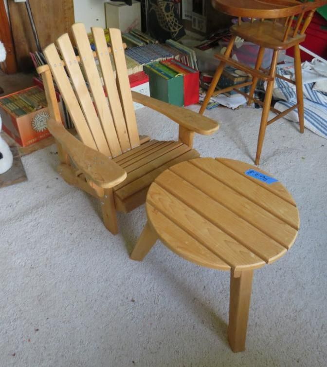 Light wood Adirondack chair and round side table on a carpeted floor.