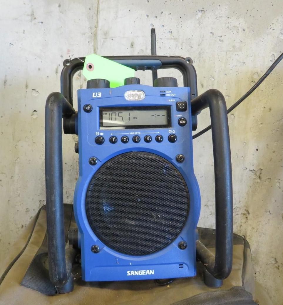 Blue SAMKAN portable radio with black handles and speaker against a concrete wall.
