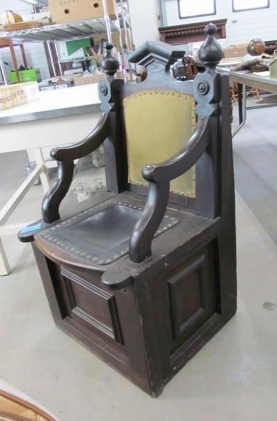 Dark wooden chair with yellow back, leather seat, and carved arms; in a workshop.