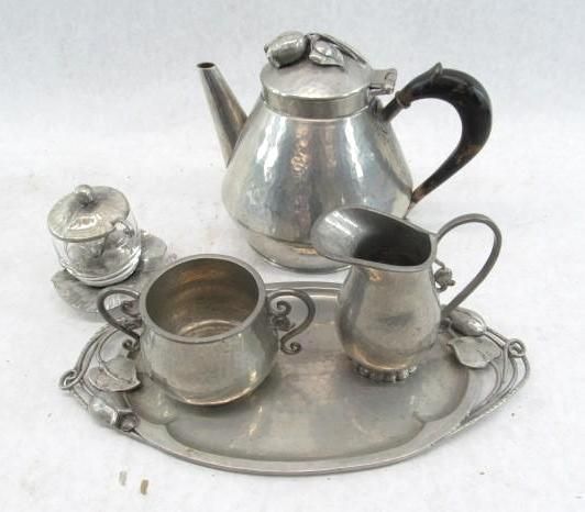 Silver tea set on tray; teapot, creamer, sugar bowl, and serving plate with leaf accents.