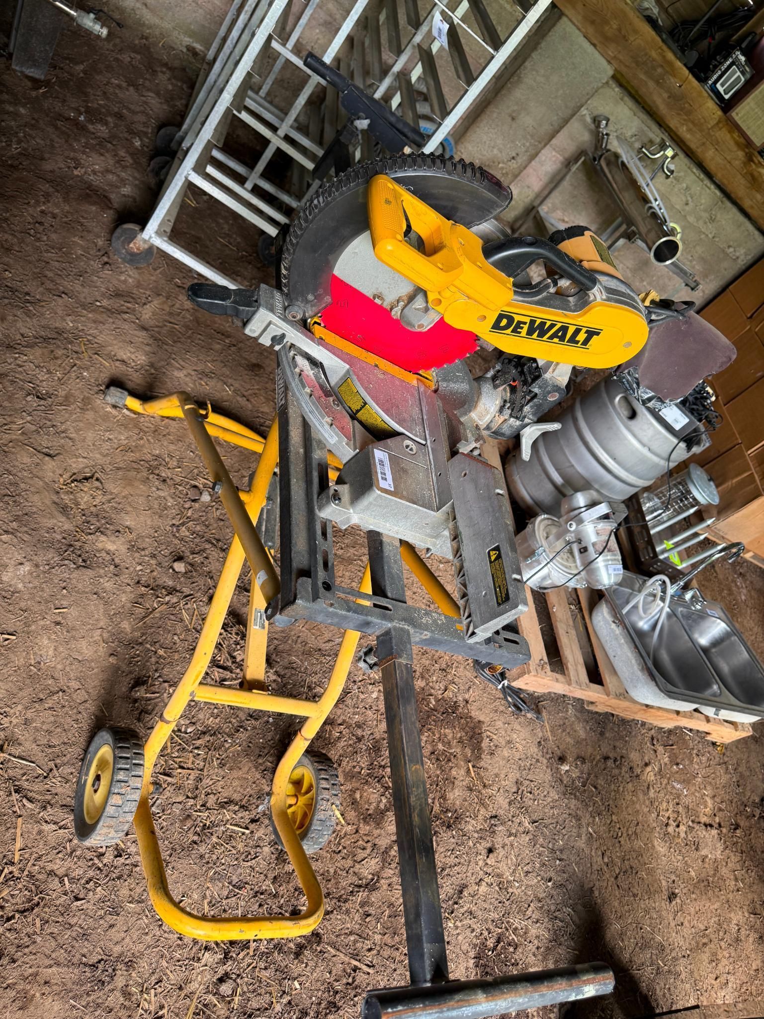 Yellow DeWalt miter saw on a rolling stand with other tools in a workshop.