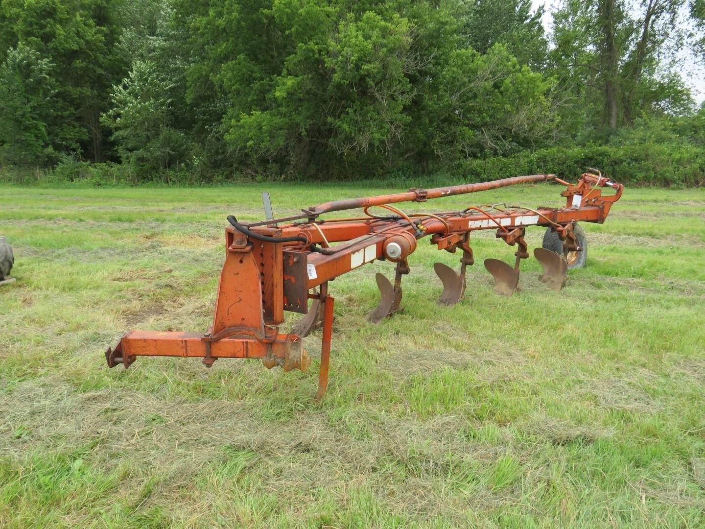 Orange plow in a field with blades facing down, trees in background.