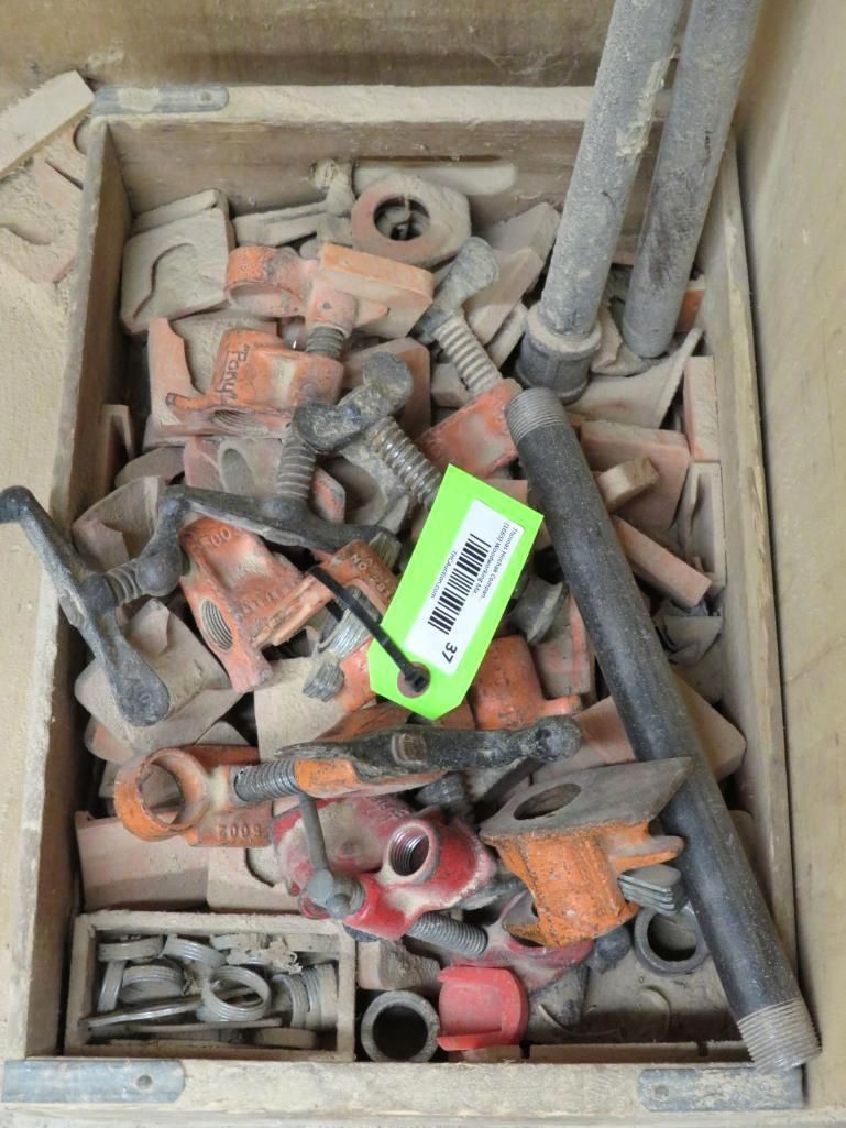 Wooden box overflowing with various orange and gray construction clamps and metal pipes.