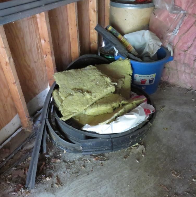 Insulation in a black bin, with other items stored near a wood-paneled wall.