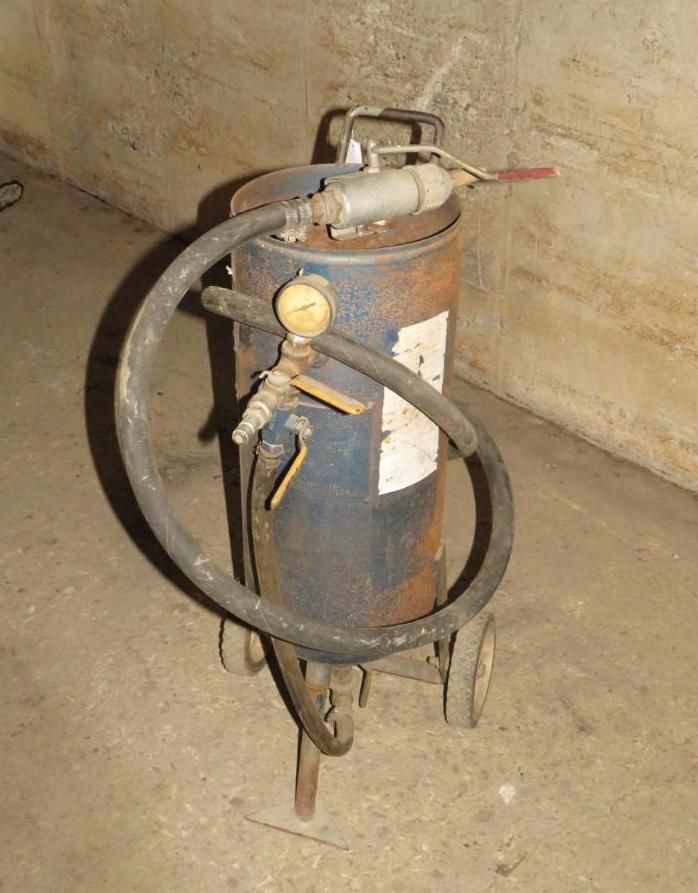 Blue sandblaster on wheels, with a hose and nozzle, in a concrete room.