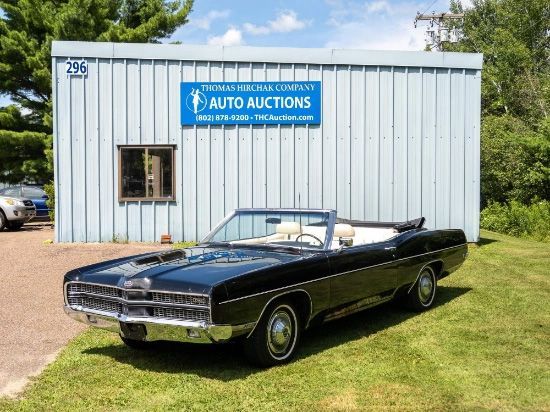 Black vintage convertible parked in front of an auto auction building on a sunny day.