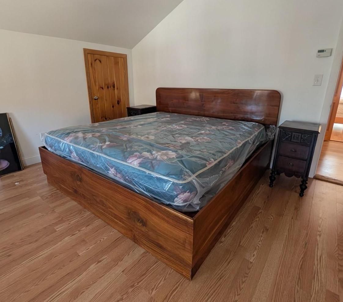 Wooden bed with blue mattress in a simple bedroom with wood floor and white walls