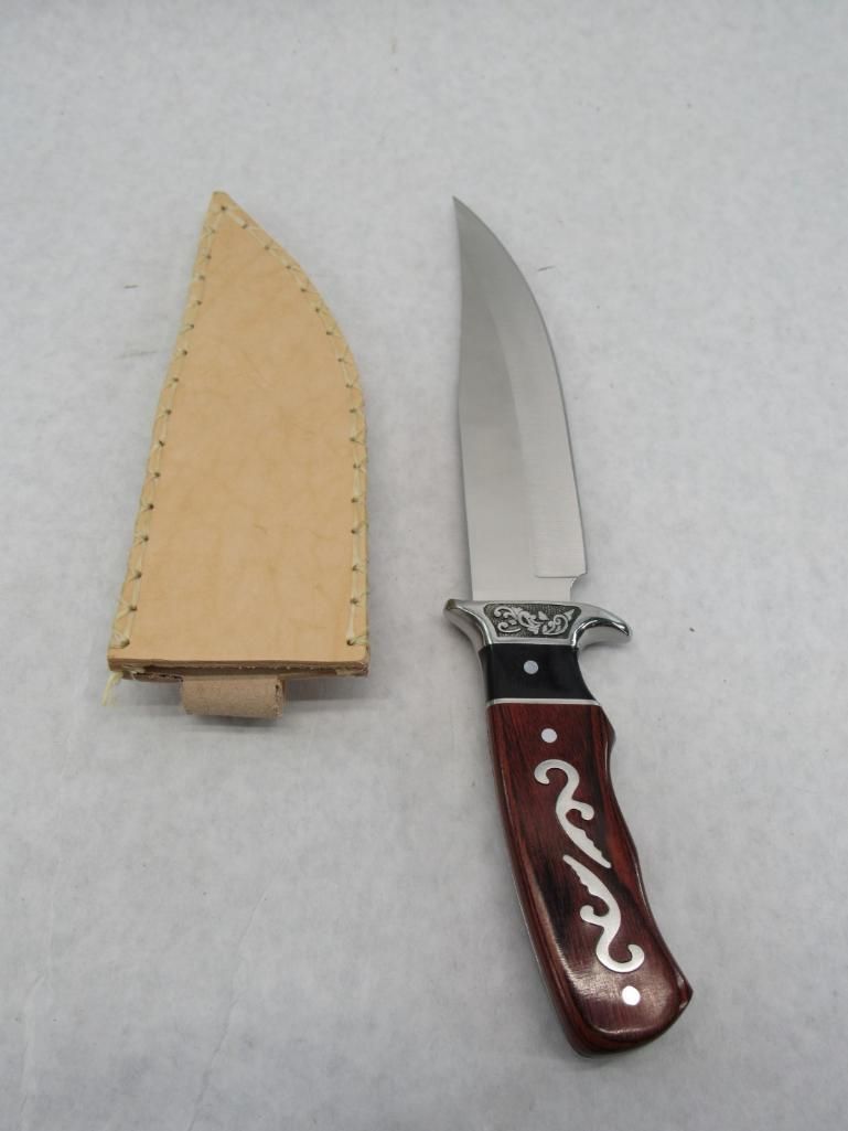 Hunting knife with leather sheath on a white surface. The knife handle is brown with silver inlays.