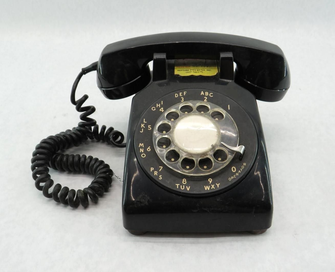 Black rotary dial telephone on a white surface. The receiver is cradled.