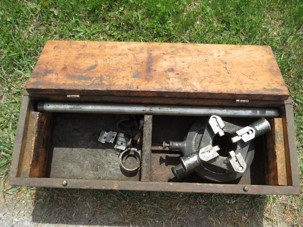 Wooden toolbox open, containing metal threading tools, pipe, and accessories.