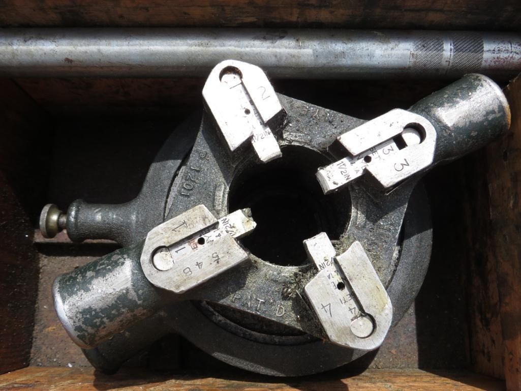 Metal adjustable reamer tool with three blades, resting in a wooden box.