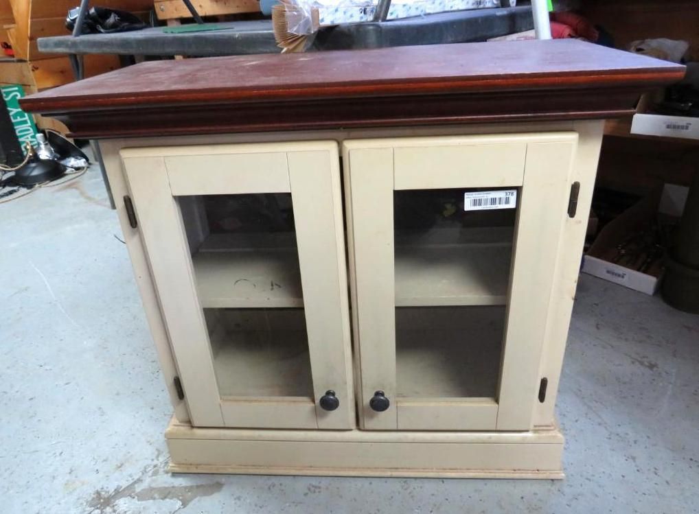A small, off-white cabinet with glass doors and a dark brown top.