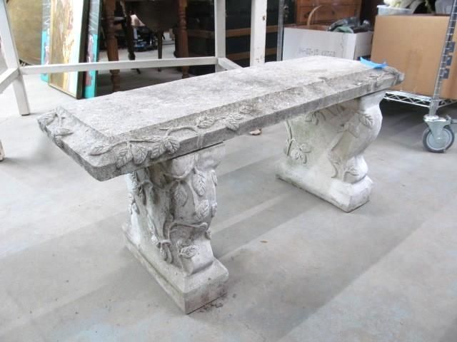Stone garden bench with decorative carved legs and top, in a light gray color.