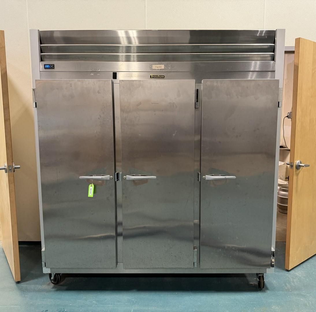 Stainless steel commercial refrigerator with three doors, flanked by wooden doors.