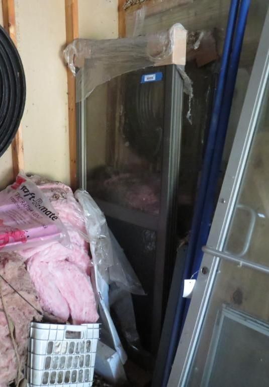 A metal appliance, wrapped in plastic, sits in a shed.