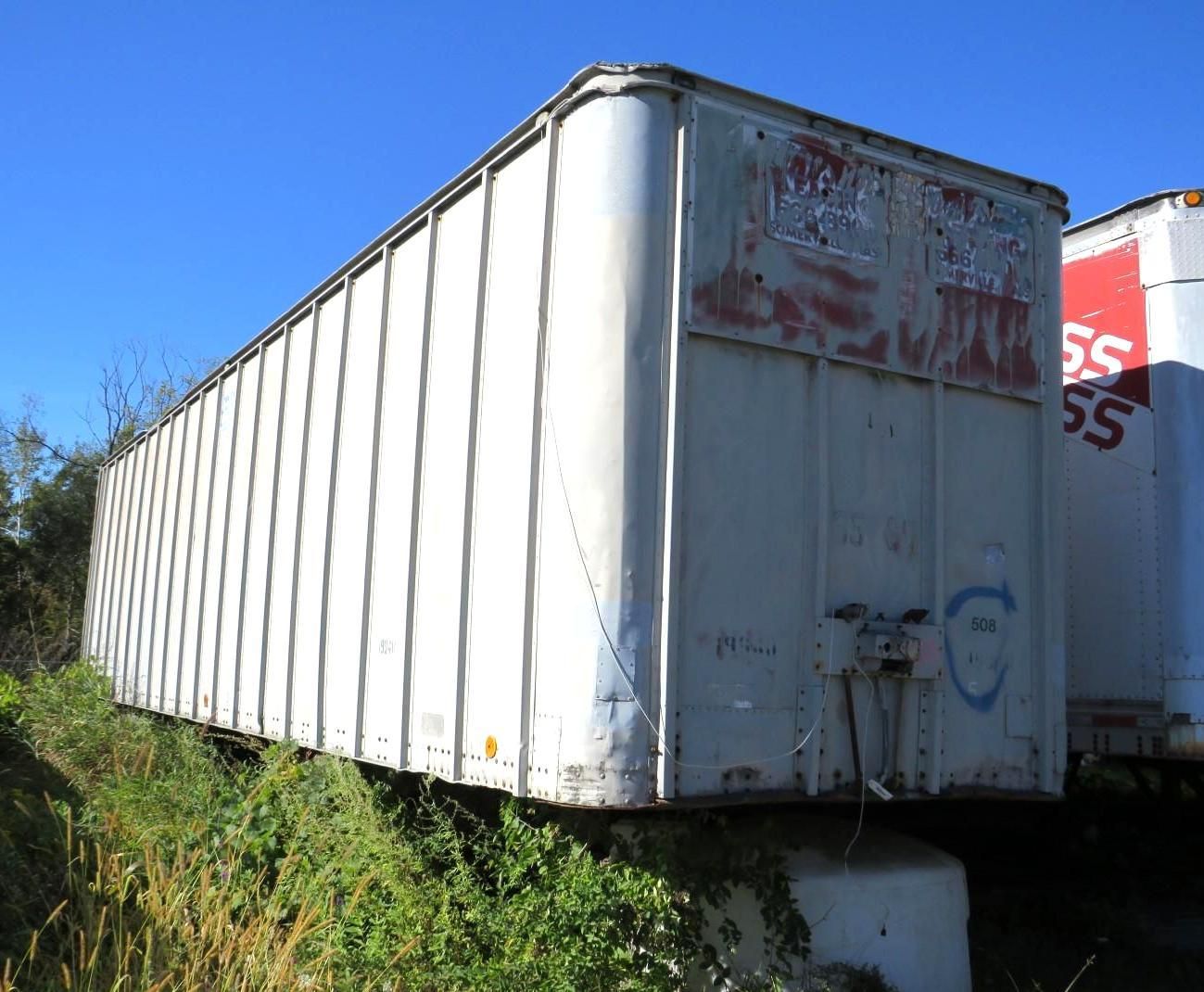 White semi-trailer, graffiti, sitting on a concrete base.