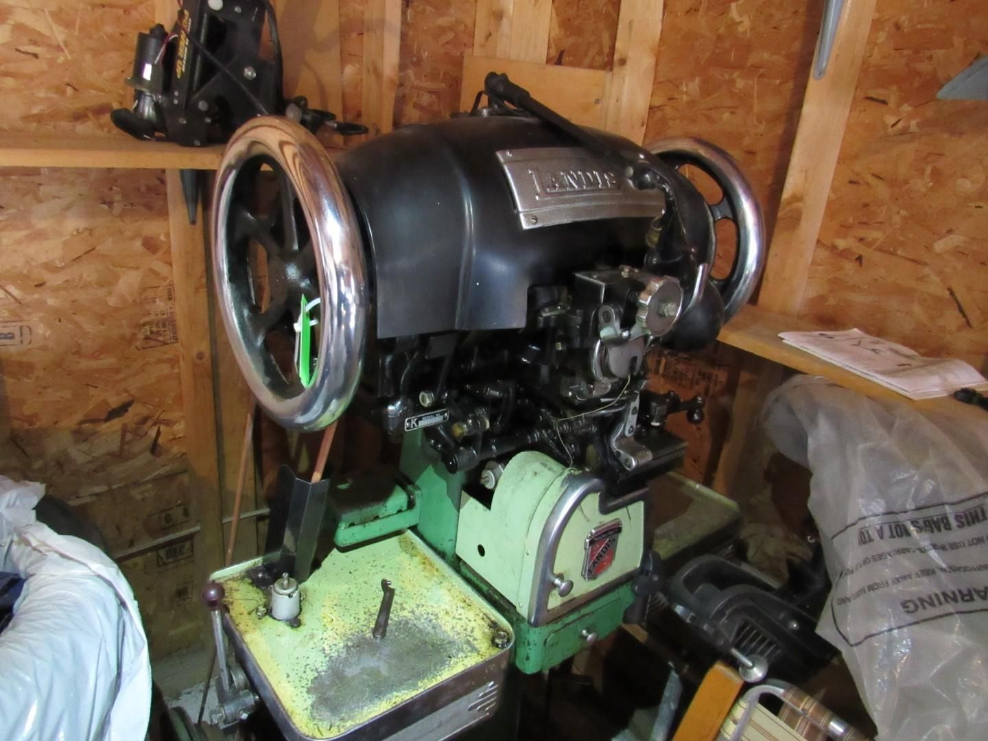 Vintage green and black industrial sewing machine in a wooden shed.