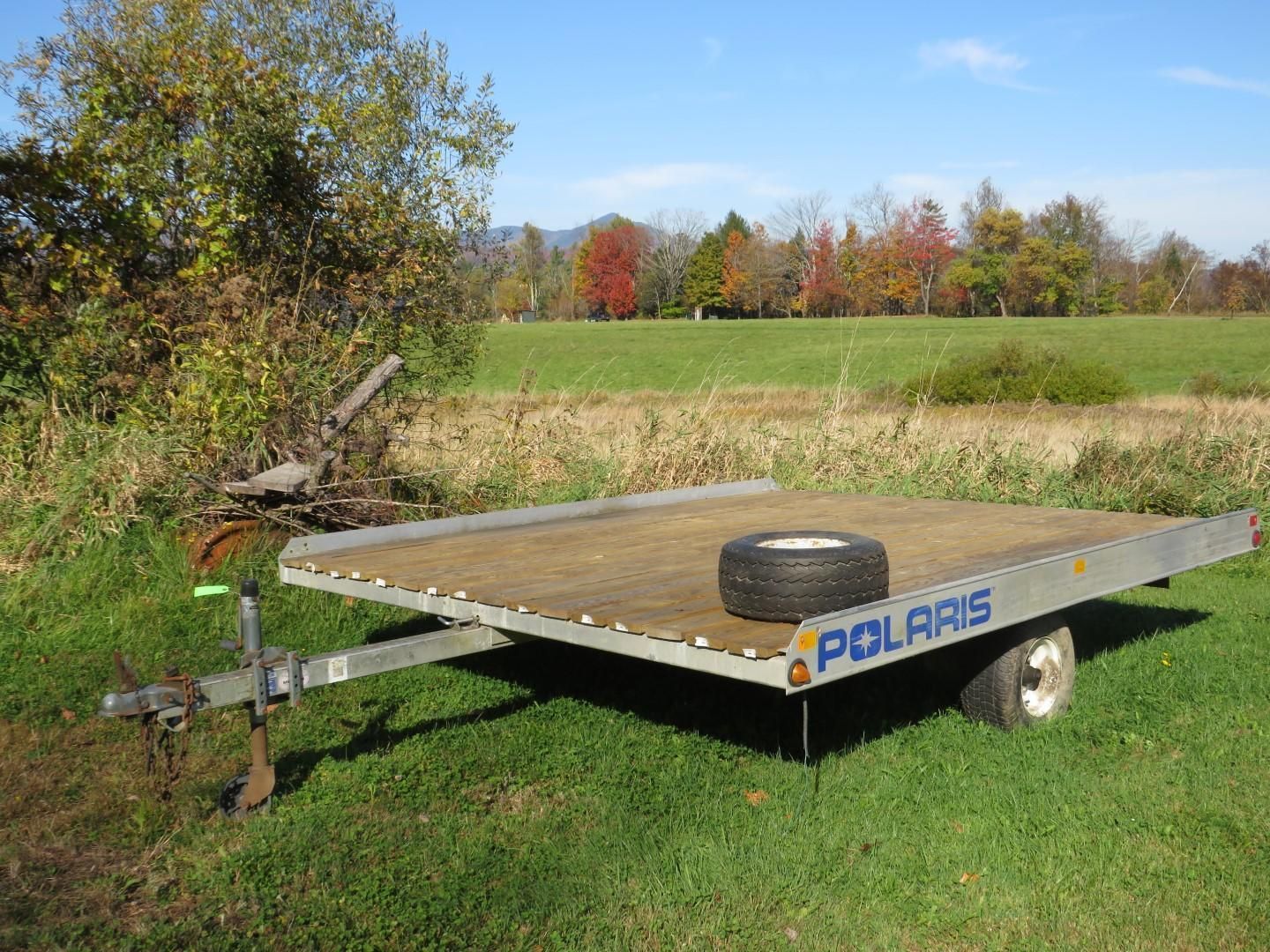 Polaris utility trailer with a spare tire on a grassy field with a backdrop of trees.