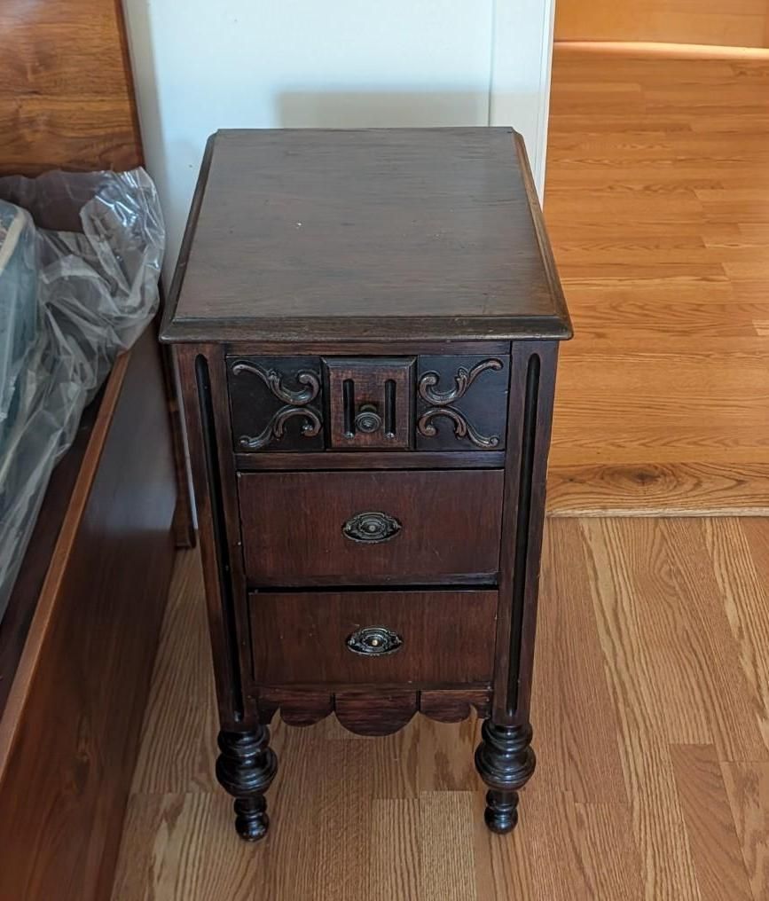 Small dark wood bedside cabinet with two drawers on a hardwood floor.