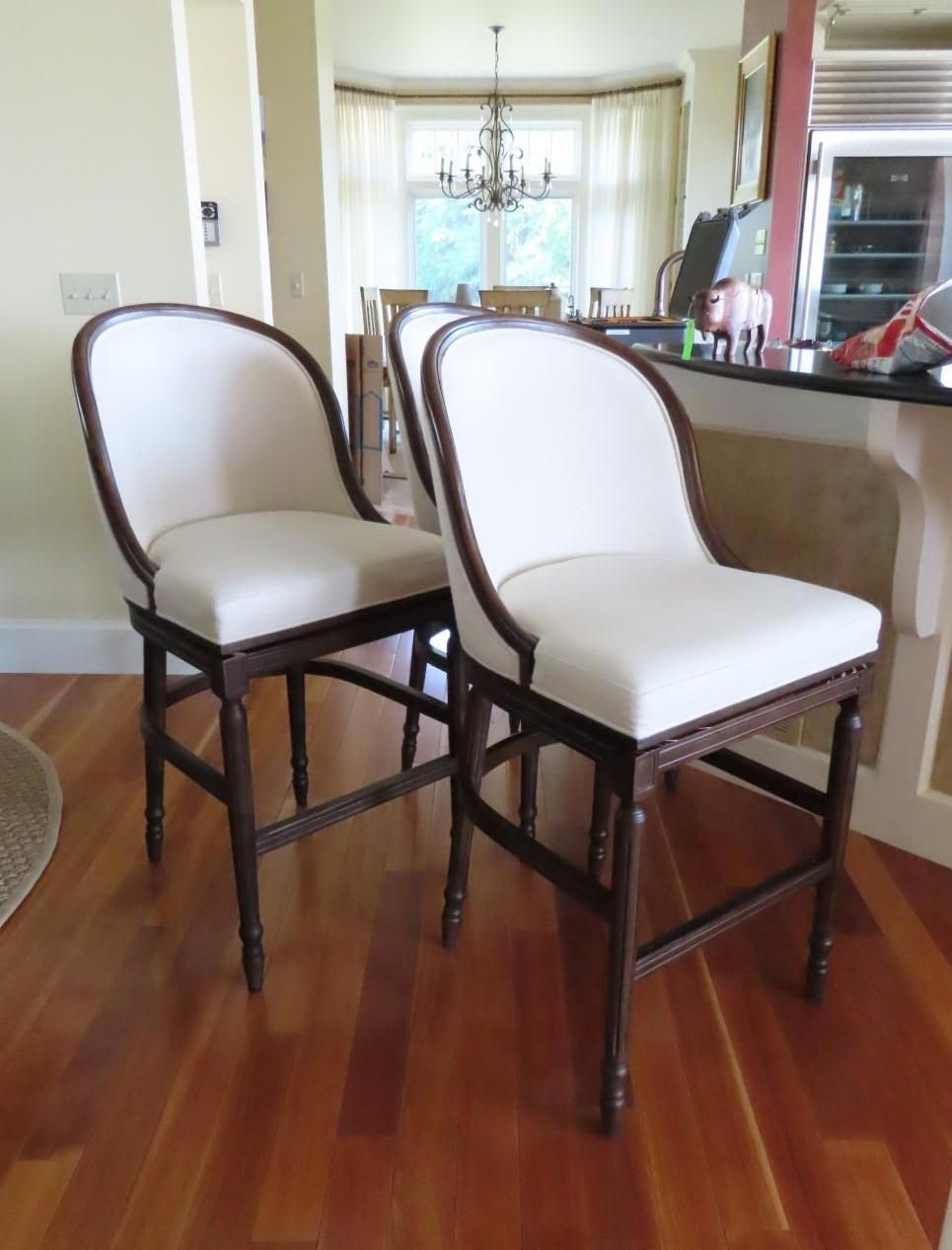 Two off-white upholstered bar stools with dark wood frames on a hardwood floor.