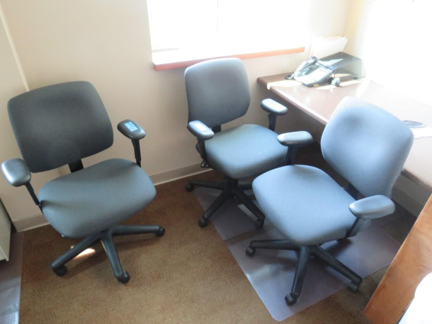 Three gray office chairs in a room with a desk.