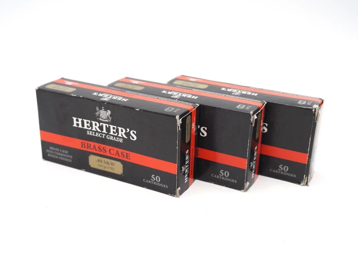 Three black and red HERTER'S brass case boxes stacked on a white background