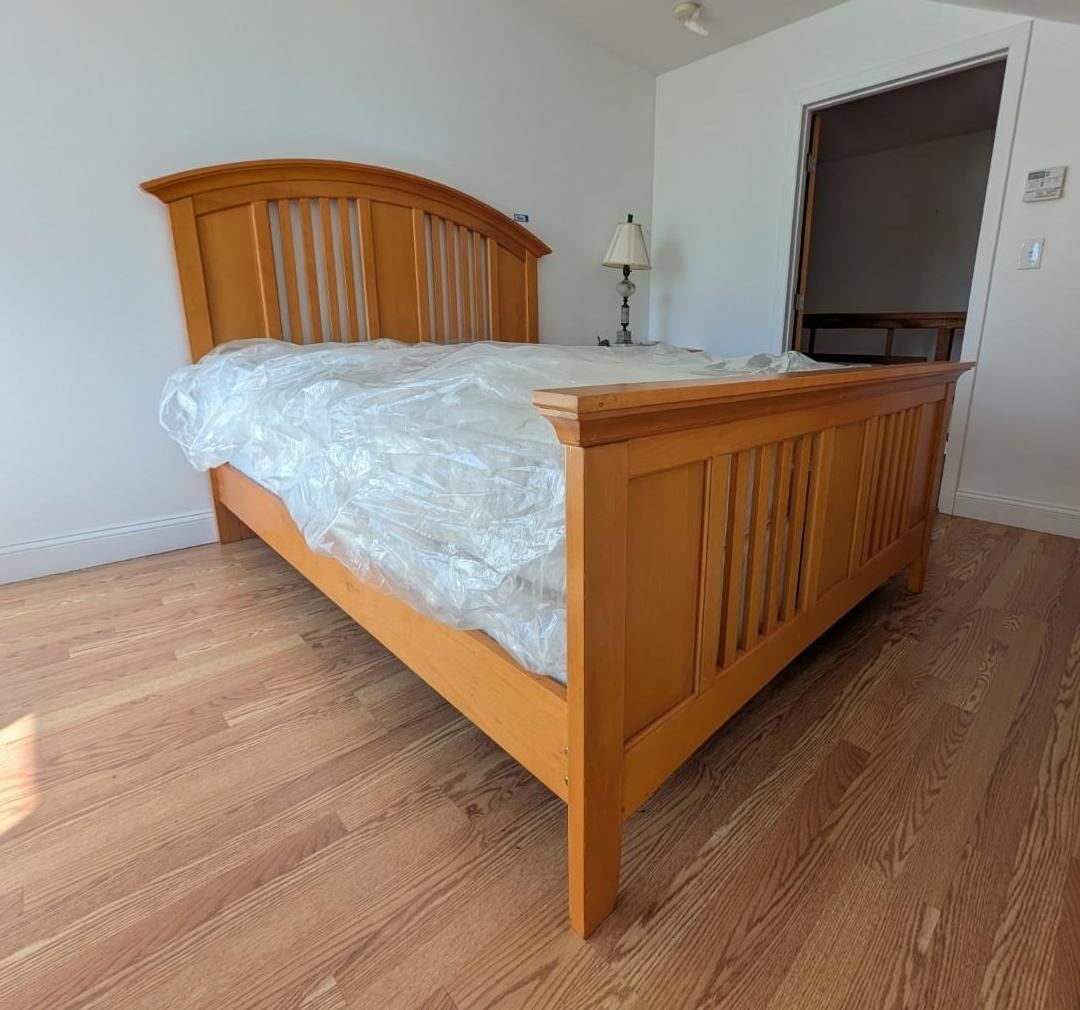 Wooden bed with white bedding in a sparsely furnished bedroom with hardwood floors