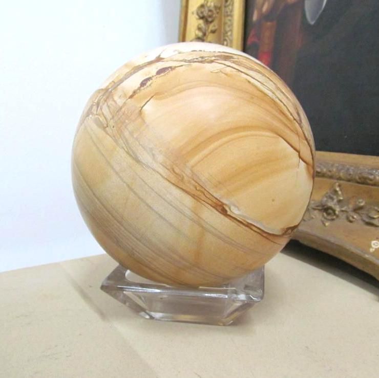 Spherical sandstone object on a clear hexagonal base, set against a blurred background.