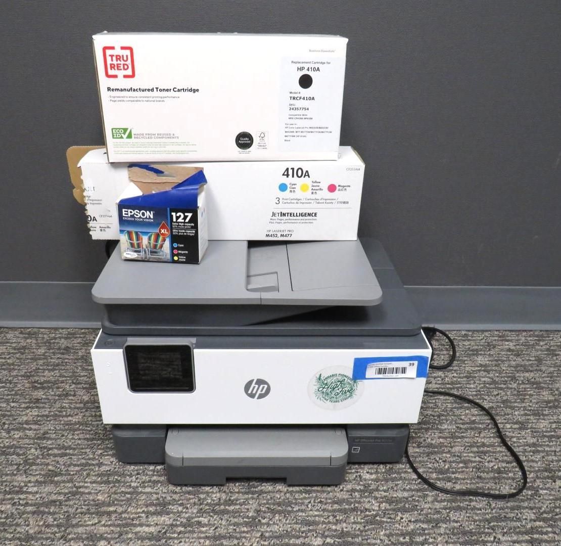 An HP printer with ink cartridges stacked on top, on a carpeted floor.