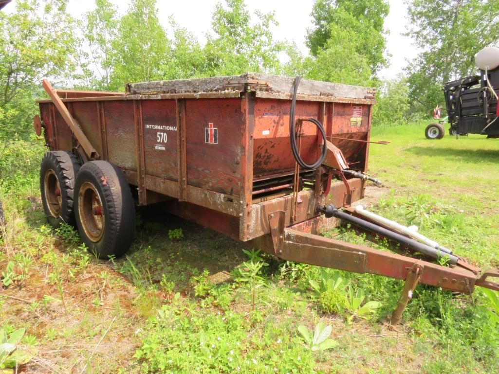 Red farm manure spreader trailer on grassy field.