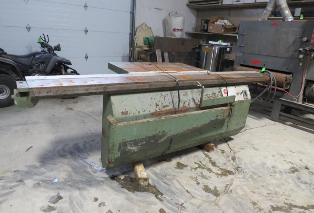 Green table saw with a long metal guide rail, in a workshop.